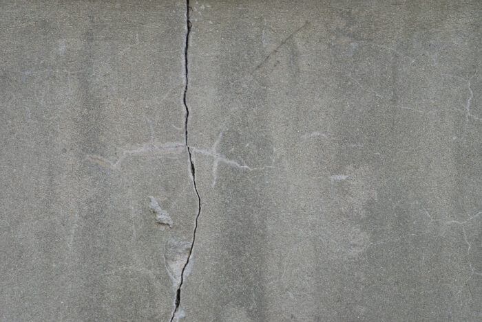 A concrete wall with a vertical crack in it that goes from the top, to the bottom of the image.